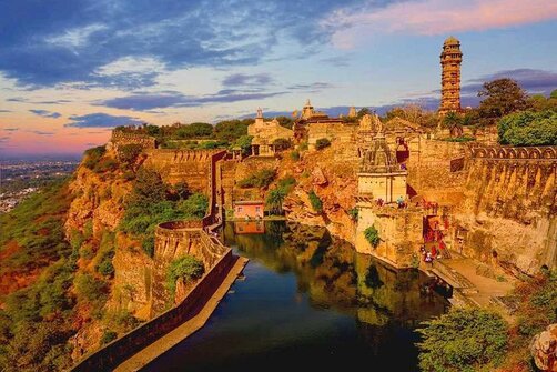 A grand view of Chittorgarh Fort at sunset, with its massive walls, structures, and a reflective body of water.