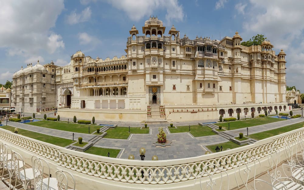 Panoramic view of the majestic City Palace in Udaipur with intricately designed architecture and well-maintained gardens under a blue sky.