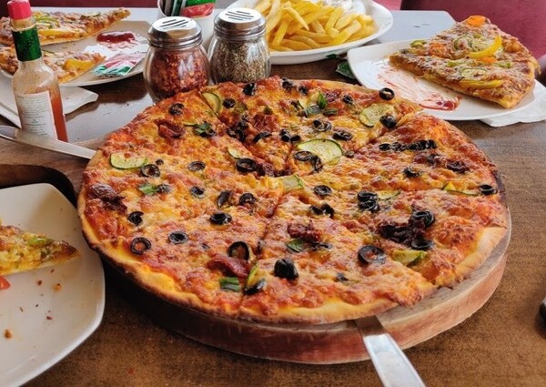 Fresh tomato pizza served on a wooden platter with a scenic lake view from Jheel’s Ginger Coffee Bar in Udaipur. 
