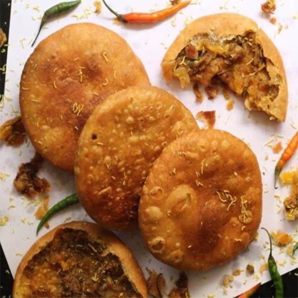 Plate with a stuffed pyaz kachori cut open, served with green and red chutneys and a red chili at Jodhpur Mishthan Bhandar.