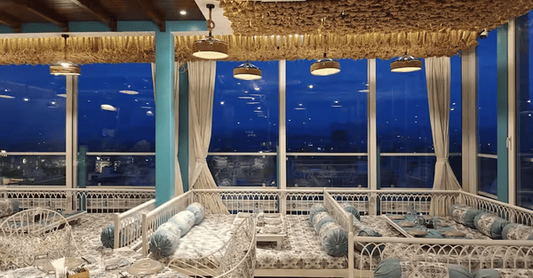 Low-floor dining setup with printed cushions and lake view at Khammaghani Restaurant in Udaipur, offering a serene waterfront ambiance. 
