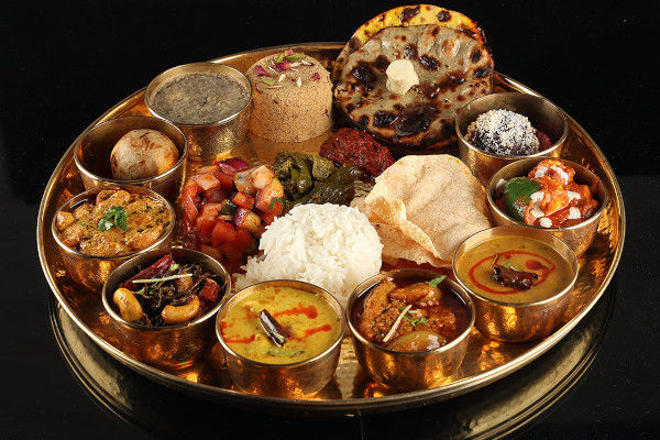Traditional Rajasthani thali served with a variety of rich curries, dal, rice, and breads on a large steel plate. 