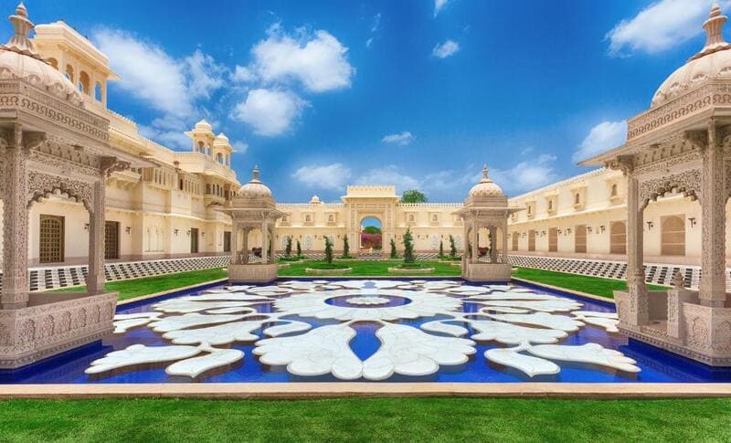 Lavish courtyard of The Oberoi Udaivilas featuring Mughal-style domes, a blue floral reflecting pool, and elegant architecture under a clear sky. 